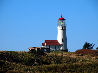 [Light is lit at this red-capped white lighthouse with an attached house. I approached it from the land side so it appears to be on flat ground as the ocean is completely hidden.]